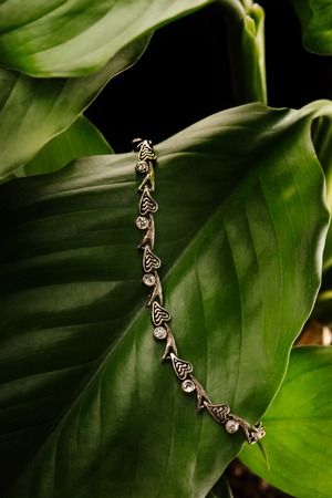 Silver wristband with diamonds layung on a green leaf, on black background