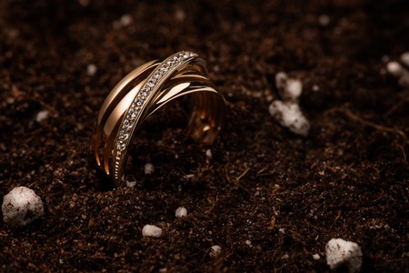 Yellow golden ring with diamonds on a creative background of brown soil with small white balls and...