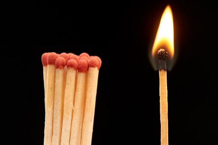 Group of red wooden matches standing with burning match, isolated on black background