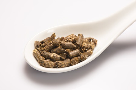 Heap of dry green medical herbal tea in white ceramic spoon on white backgroundの写真素材