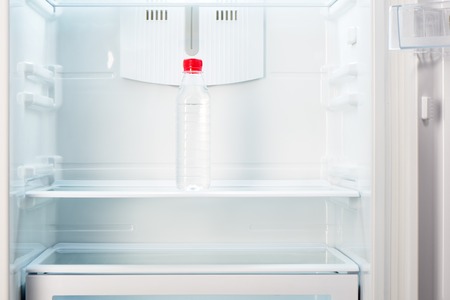 Bottle of water on shelf of open empty refrigerator. Weight loss diet concept.の写真素材