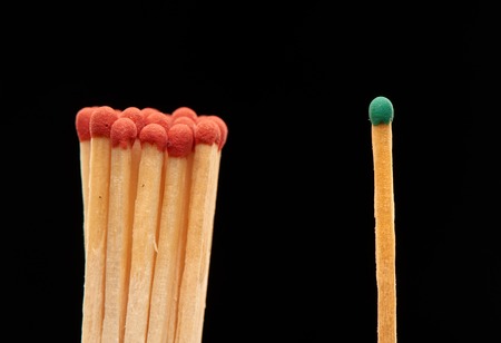 Group of red wooden matches standing with green match, isolated on black backgroundの写真素材