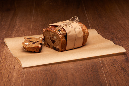 Sliced fruit bread with raisins, prunes and nuts in baking paper on dark wooden table background