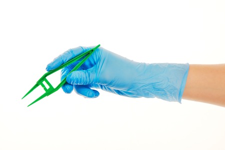 Close up of female doctor's hand in blue sterilized surgical glove with green plastic forceps against white backgroundの写真素材
