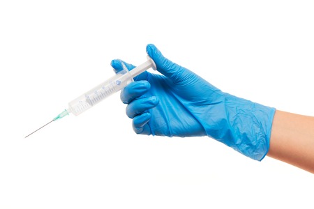 Close up of female doctor's hand in blue sterilized surgical glove with plastic medical syringe against white backgroundの写真素材