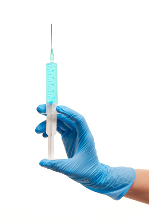 Close up of female doctor's hand in blue sterilized surgical glove with plastic medical syringe filled with blue drug against white backgroundの写真素材
