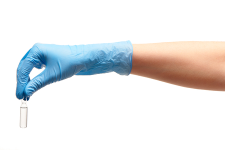 Close up of female doctor's hand in blue sterilized surgical glove holding transparent white glass ampoule with a drug against white backgroundの写真素材