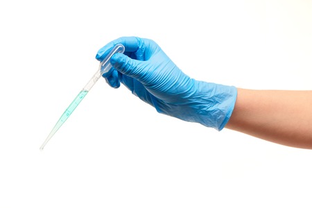 Close up of female doctor's hand in blue sterilized surgical glove with white plastic medical dropper filled with blue drug against white backgroundの写真素材