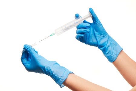 Close up of female doctor's hands in blue sterilized surgical gloves with plastic medical syringe against white backgroundの写真素材