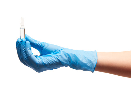 Close up of female doctor's hand in blue sterilized surgical glove holding transparent white glass ampoule with a drug against white backgroundの写真素材