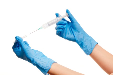 Close up of female doctor's hands in blue sterilized surgical gloves with plastic medical syringe against white backgroundの写真素材