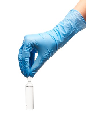 Close up of female doctor's hand in blue sterilized surgical glove holding transparent white glass ampoule with a drug against white backgroundの写真素材