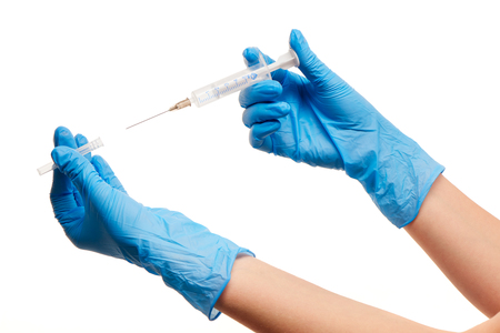 Close up of female doctor's hands in blue sterilized surgical gloves with plastic medical syringe against white backgroundの写真素材