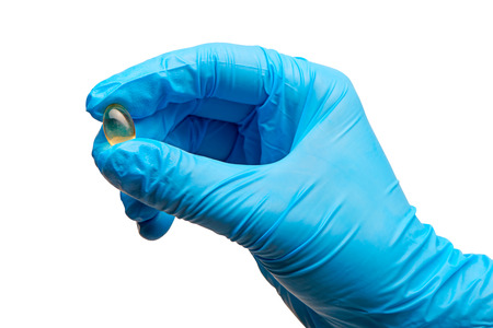 Close up of female doctor's hand in blue sterilized surgical glove holding yellow tablet against white backgroundの写真素材