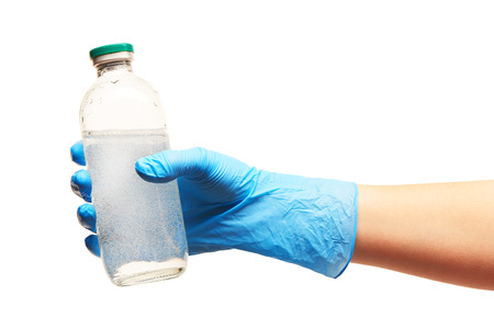 Close up of female doctor's hand in blue sterilized surgical glove holding transparent white glass bottle for medicines with a drug against white backgroundの写真素材