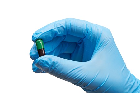 Close up of female doctor's hand in blue sterilized surgical glove holding green and black capsule against white backgroundの写真素材