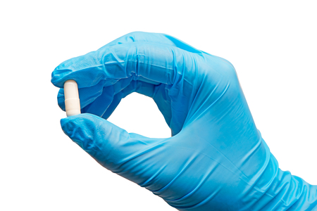 Close up of female doctor's hand in blue sterilized surgical glove holding white capsule against white backgroundの写真素材