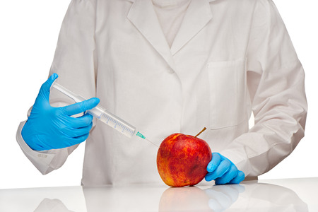 Close up of female doctor in white medical gown and blue sterilized surgical gloves makes injection to bad looking apple with plastic syringeの写真素材