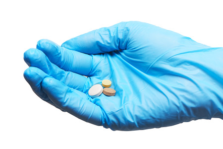Close up of three round white, yellow and brown tablets on female doctor's hand in blue sterilized surgical glove against white backgroundの写真素材
