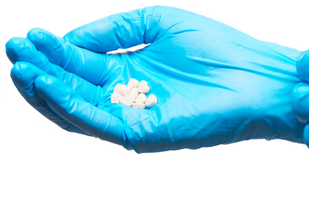 Close up of pile of white heart shape tablets on female doctor's hand in blue sterilized surgical...