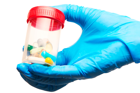 Close up of female doctor's hand in blue sterilized surgical glove holding transparent plastic sterile specimen collection container filled with different tablets and capsules against white backgroundの写真素材