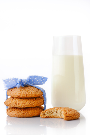 Stack of three homemade oatmeal cookies tied with blue ribbon in small white polka dots, bitten cookie and glass of milk, isolated on white backgroundの写真素材