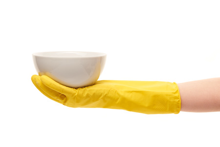 Close up of female hand in yellow protective rubber glove holding clean white bowl against white background.の写真素材