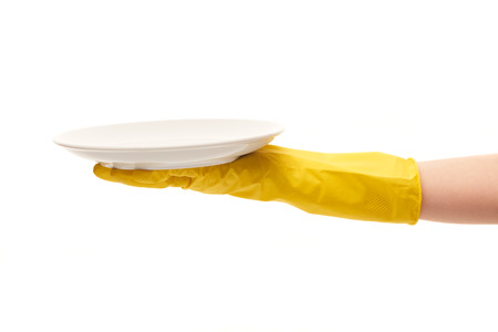 Close up of female hand in yellow protective rubber glove holding clean white plate against white background. の写真素材