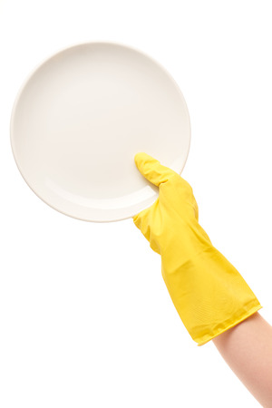 Close up of female hand in yellow protective rubber glove holding clean white plate against white backgroundの写真素材