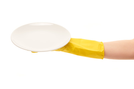 Close up of female hand in yellow protective rubber glove holding clean white plate against white background. の写真素材