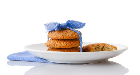 Stack of three homemade oatmeal cookies tied with blue ribbon in small white polka dots and bitten cookie on white ceramic plate on matching blue napkin, isolated on white backgroundの写真素材
