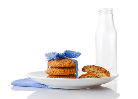 Stack of three homemade oatmeal cookies tied with blue ribbon in small white polka dots and halves of cookies on white plate on napkin and empty milk bottle, isolated on white backgroundの写真素材