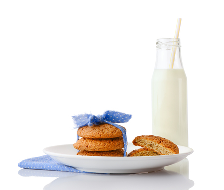 Stack of three homemade oatmeal cookies tied with blue ribbon in small white polka dots and halves of cookies on white plate on napkin and bottle of milk with straw, isolated on white backgroundの写真素材