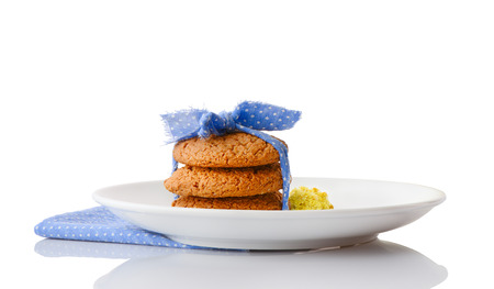 Stack of three homemade oatmeal cookies tied with blue ribbon in small white polka dots and tiny yellow flowers on white ceramic plate on matching blue napkin, isolated on white backgroundの写真素材