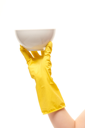Close up of female hand in yellow protective rubber glove holding clean white bowl against white backgroundの写真素材