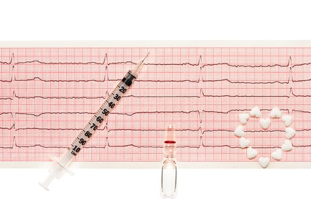 Heart made of white heart shape tablets, transparent white glass ampoule with a drug and plastic syringe with open needle on paper ECG results isolated on white background.の写真素材