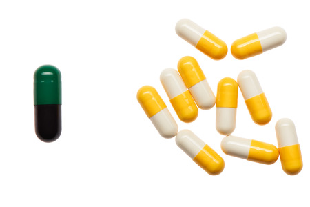 Pile of yellow and white capsules and one bigger green and black capsule isolated on white background. Clipping path included.の写真素材