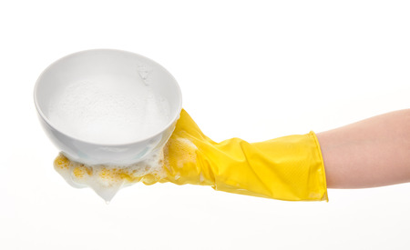 Close up of female hand in yellow protective rubber glove holding clean white bowl in foam against white backgroundの写真素材