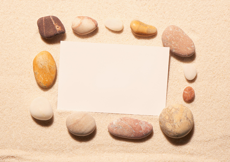 Rectangular frame of sea stones with blank white visit card on sand. Summer beach background. View from aboveの写真素材