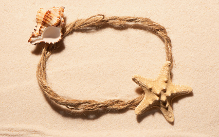 Oval frame of rope with starfish and empty sea shell on sand. Summer beach background. View from aboveの写真素材
