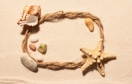 Oval frame of rope with starfish, empty sea shell and stones on sand. Summer beach background. View from aboveの写真素材