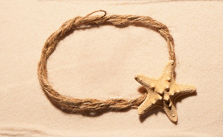 Oval frame of rope with starfish on sand. Summer beach background. View from aboveの写真素材