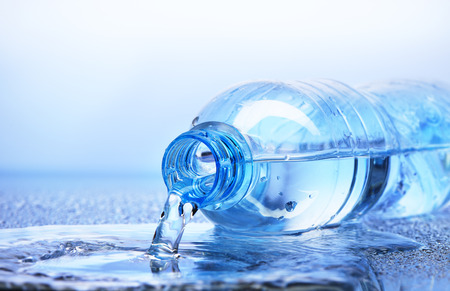 Water pouring from plastic bottle with reflection on white and blue backgroundの写真素材