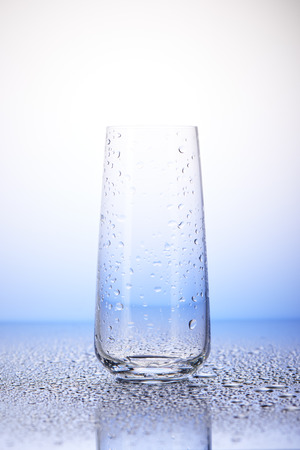 Empty drinking glass with reflection in drops of water on white and blue backgroundの写真素材
