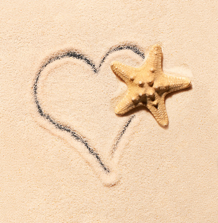 Starfish on sand and heart drawn on sand. Summer beach background. View from aboveの写真素材