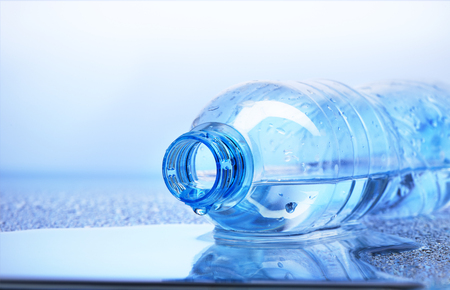 Drop of water falling from plastic bottle with reflection on white and blue backgroundの写真素材