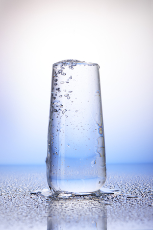 Full drinking glass with reflection in drops of water on white and blue backgroundの写真素材