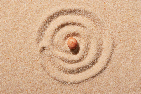 Spiral drawn on beach sand with pink round sea stone in centre. Summer beach background. View from aboveの写真素材