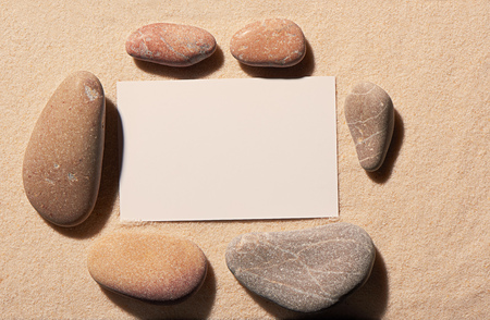 Rectangular frame of six small and large sea stones with blank white visit card on sand. Summer beach background. View from aboveの写真素材