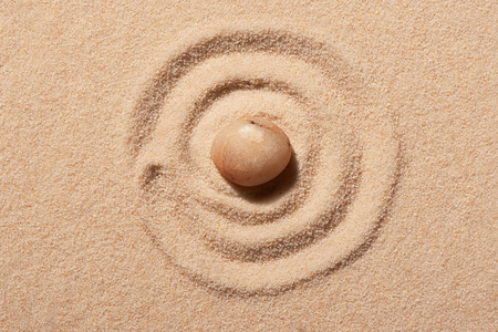 Spiral drawn on beach sand with pink round sea stone in centre. Summer beach background. View from...